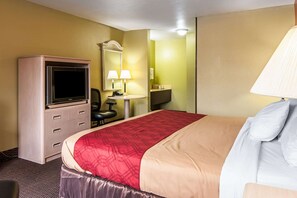 A hotel room with a bed, a desk with a computer, a television, and a mirror.
