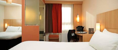 A hotel room with a large bed, a desk with a chair, a small table, and a mirror.