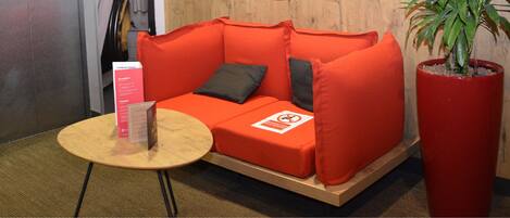 A red sofa with a small table and a sign, a potted plant, and a wooden wall.