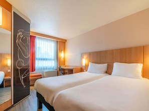 Quarto de hotel com uma cama grande, uma escrivaninha, uma cadeira e uma janela com cortinas.