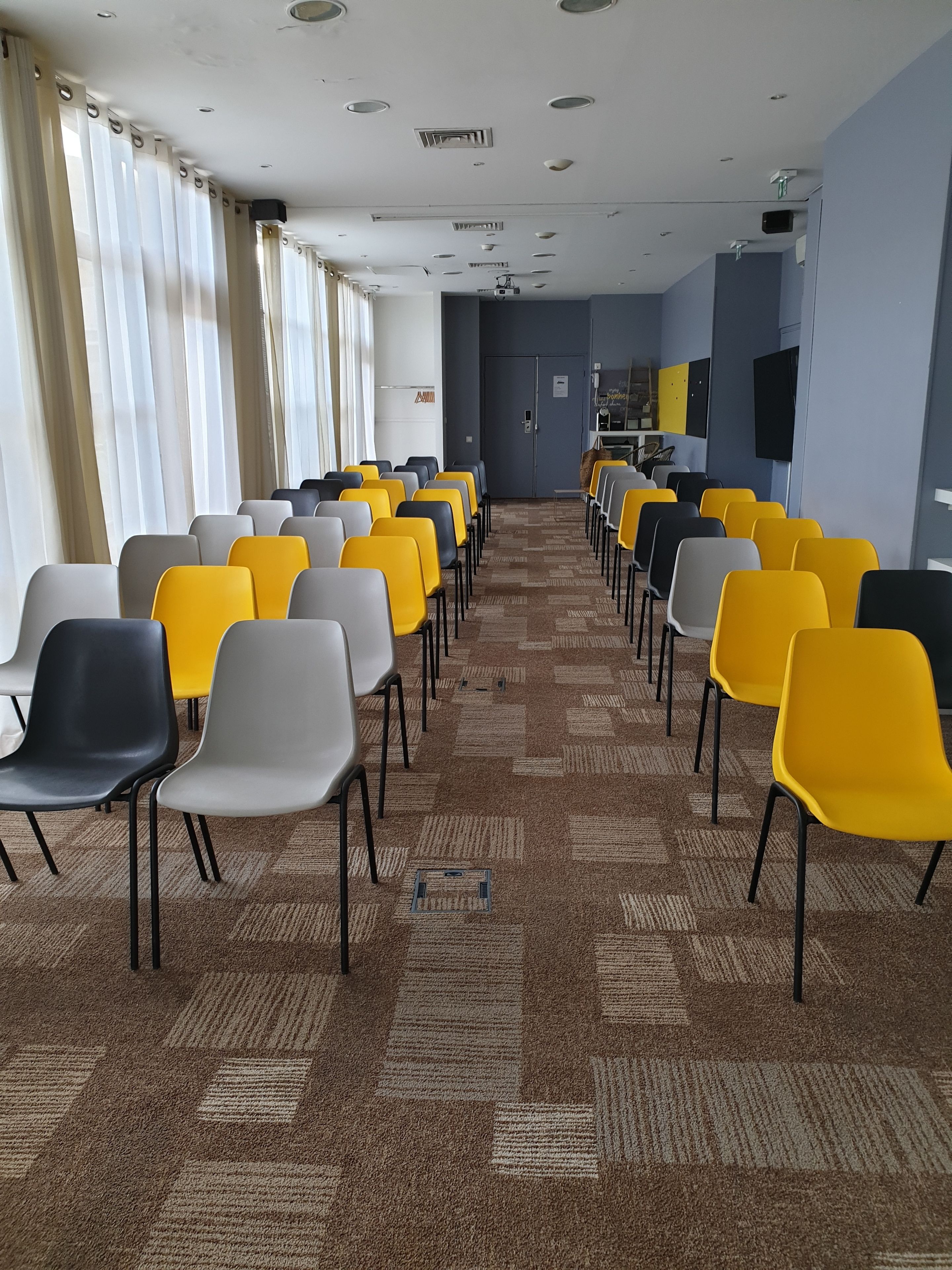 Ein Konferenzraum mit Reihen von Stühlen, einem Teppichboden und einer Projektionsleinwand an der Wand.