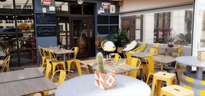 An outdoor seating area with yellow chairs and tables, a cactus centerpiece, and a menu board on the wall.