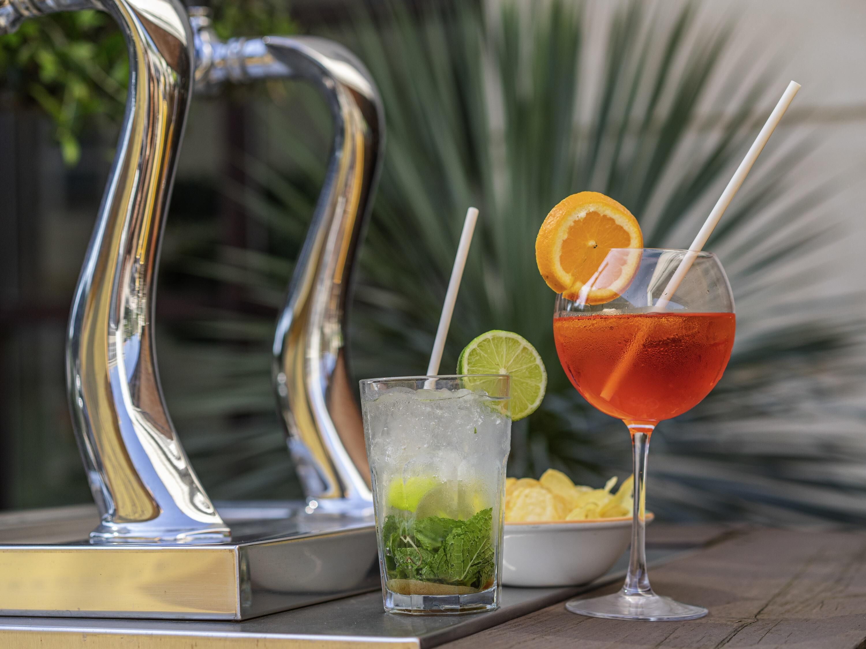 Una mesa con dos bebidas, una con rodaja de lima y menta, y otra con rodaja de naranja.
