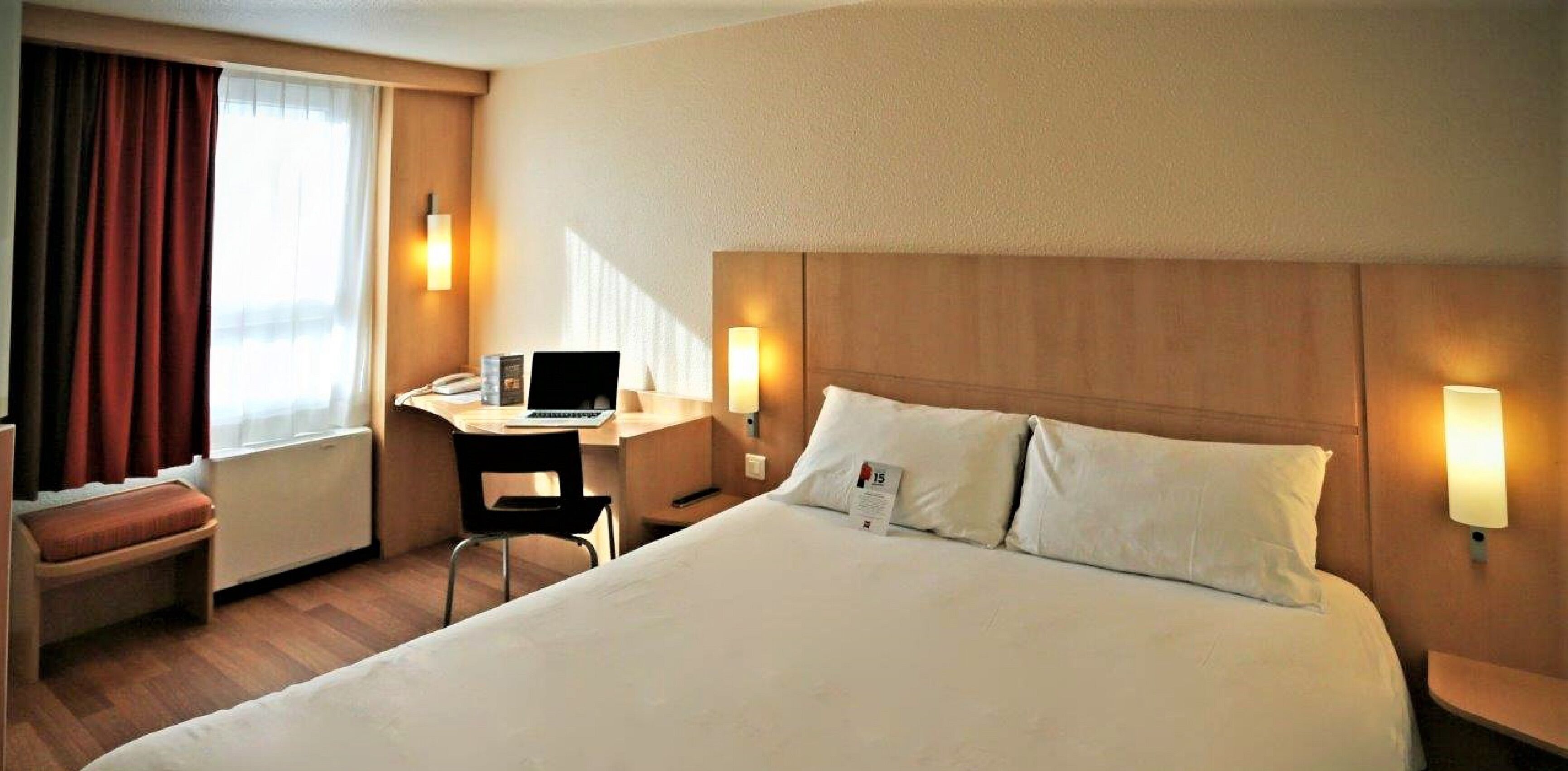 Une chambre d’hôtel avec un grand lit, un bureau avec un ordinateur portable, une chaise et deux lampes de chevet.