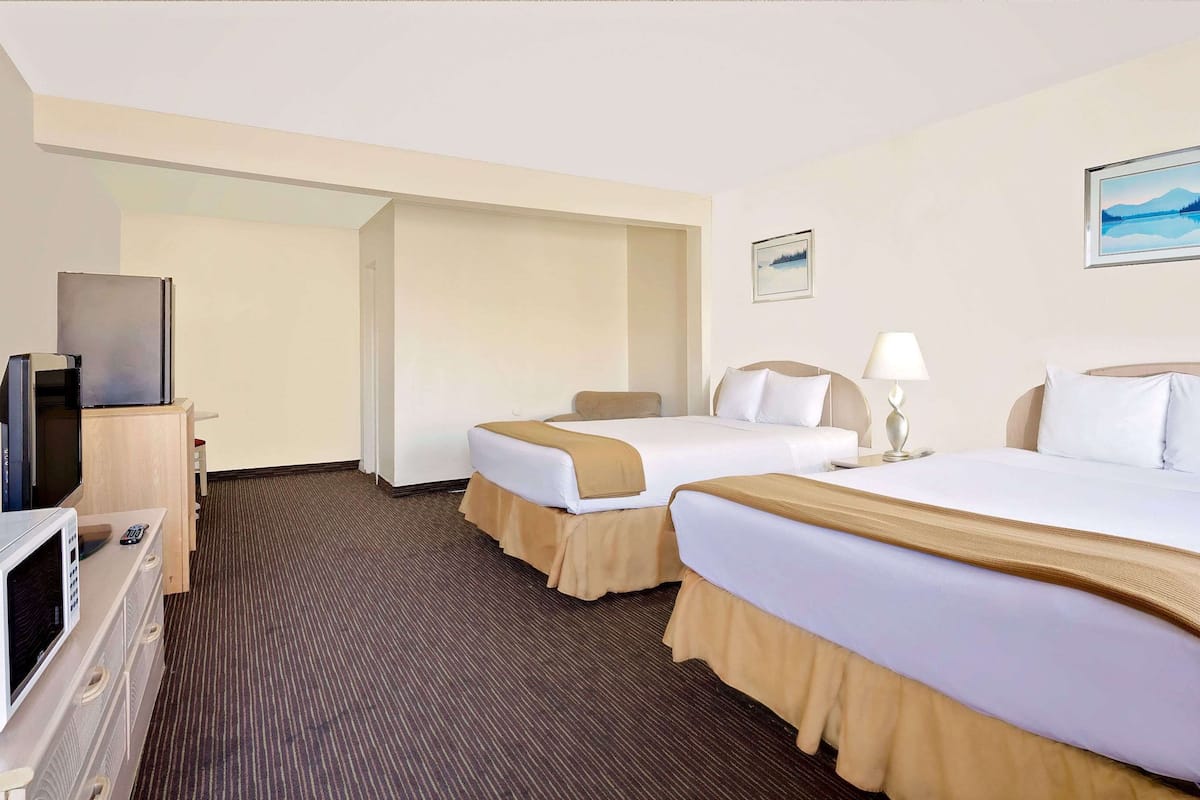 A hotel room with two beds, a TV, a microwave, and a painting on the wall.