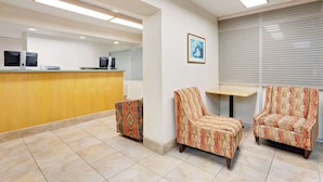 A hotel lobby with a reception desk, two patterned armchairs, a small table, and a framed picture on the wall. - Knights Inn Page (Page)
