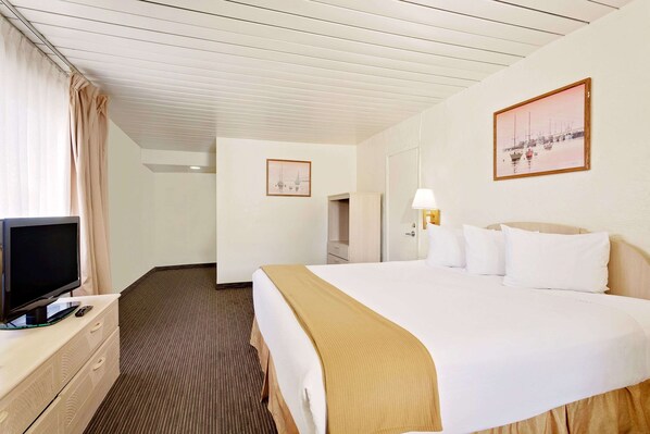 Una habitación de hotel con una cama, un televisor en una cómoda, una lámpara y dos cuadros en la pared.