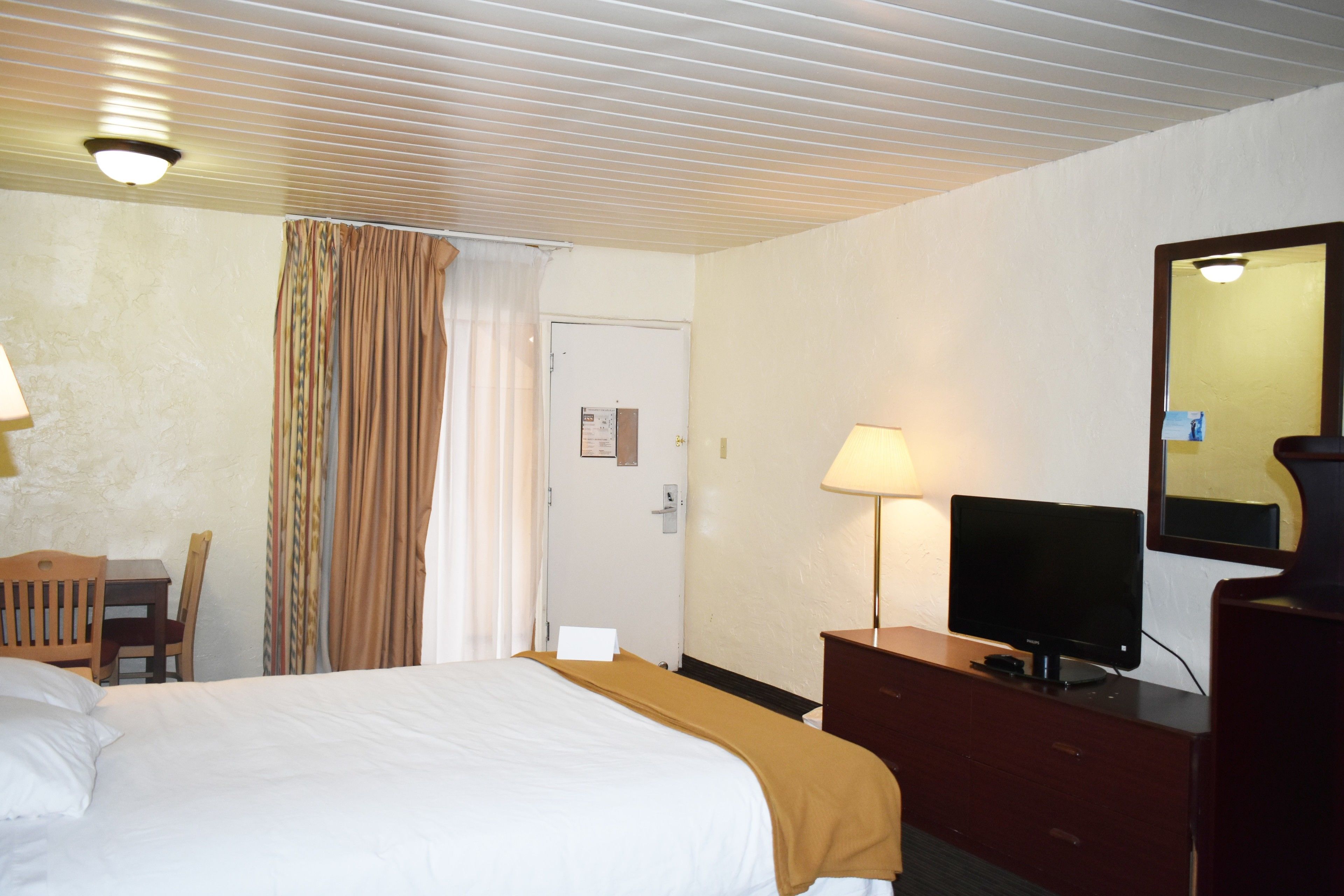 A hotel room with a bed, a desk with a chair, a television, and a dresser.