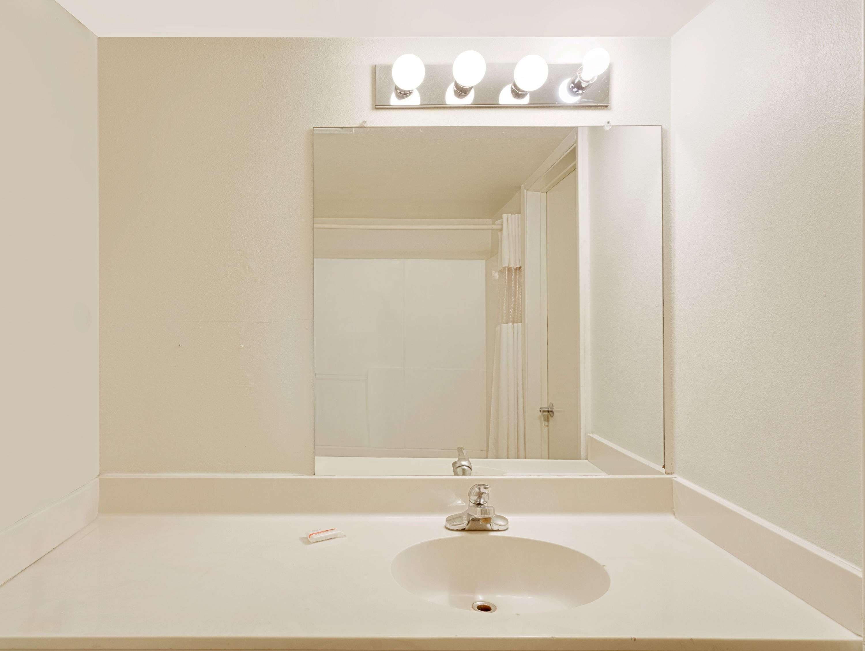 A bathroom with a white sink, a mirror with lights, and a door in the background.