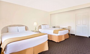 A hotel room with two beds, a small table, a chair, a lamp, and a door.
