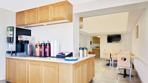 A modern kitchen with wooden cabinets, a coffee machine, and a microwave. There is a dining area with chairs and a table. - Knights Inn Page (Page)