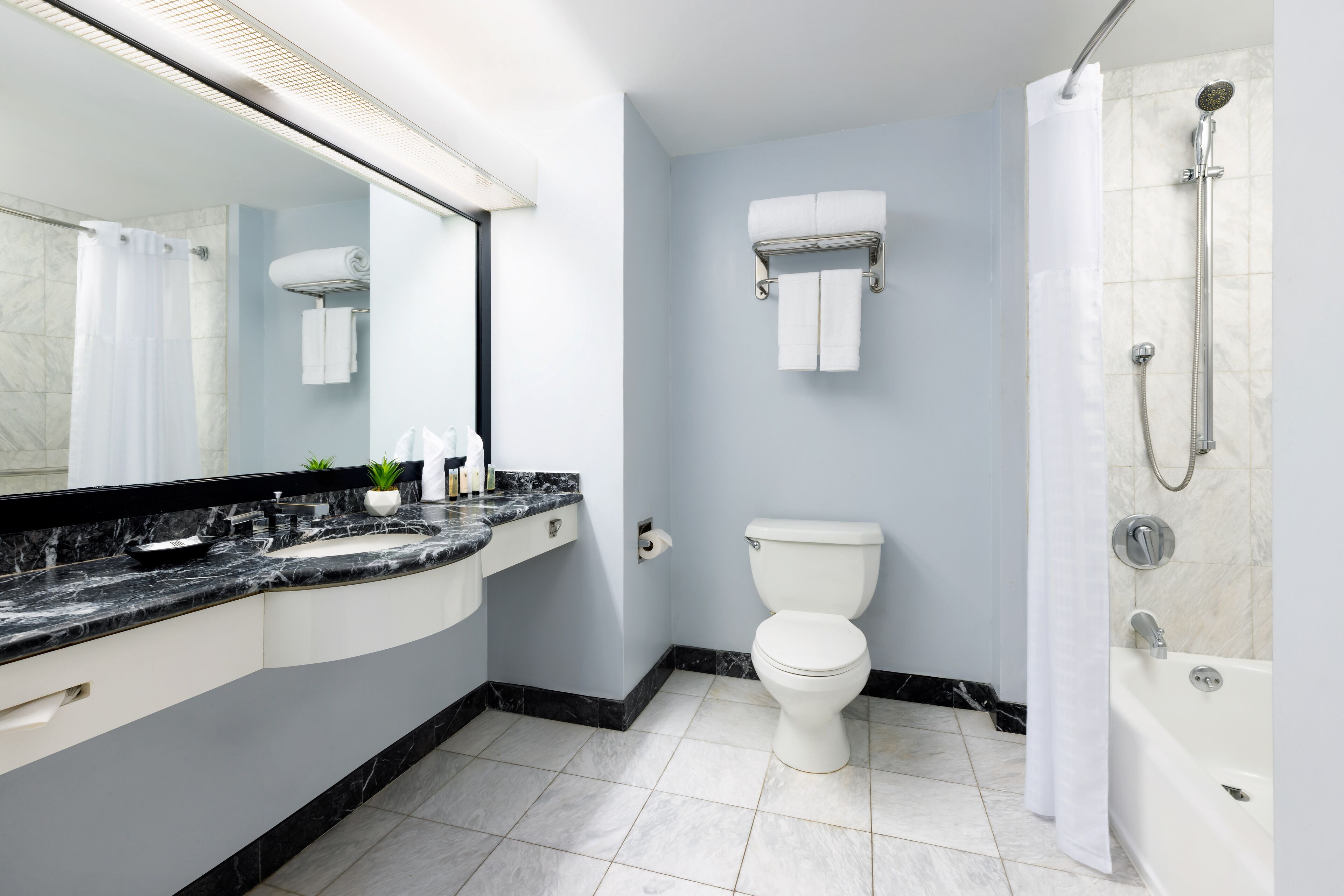A modern bathroom with a marble countertop, a toilet, a shower, and a towel rack.