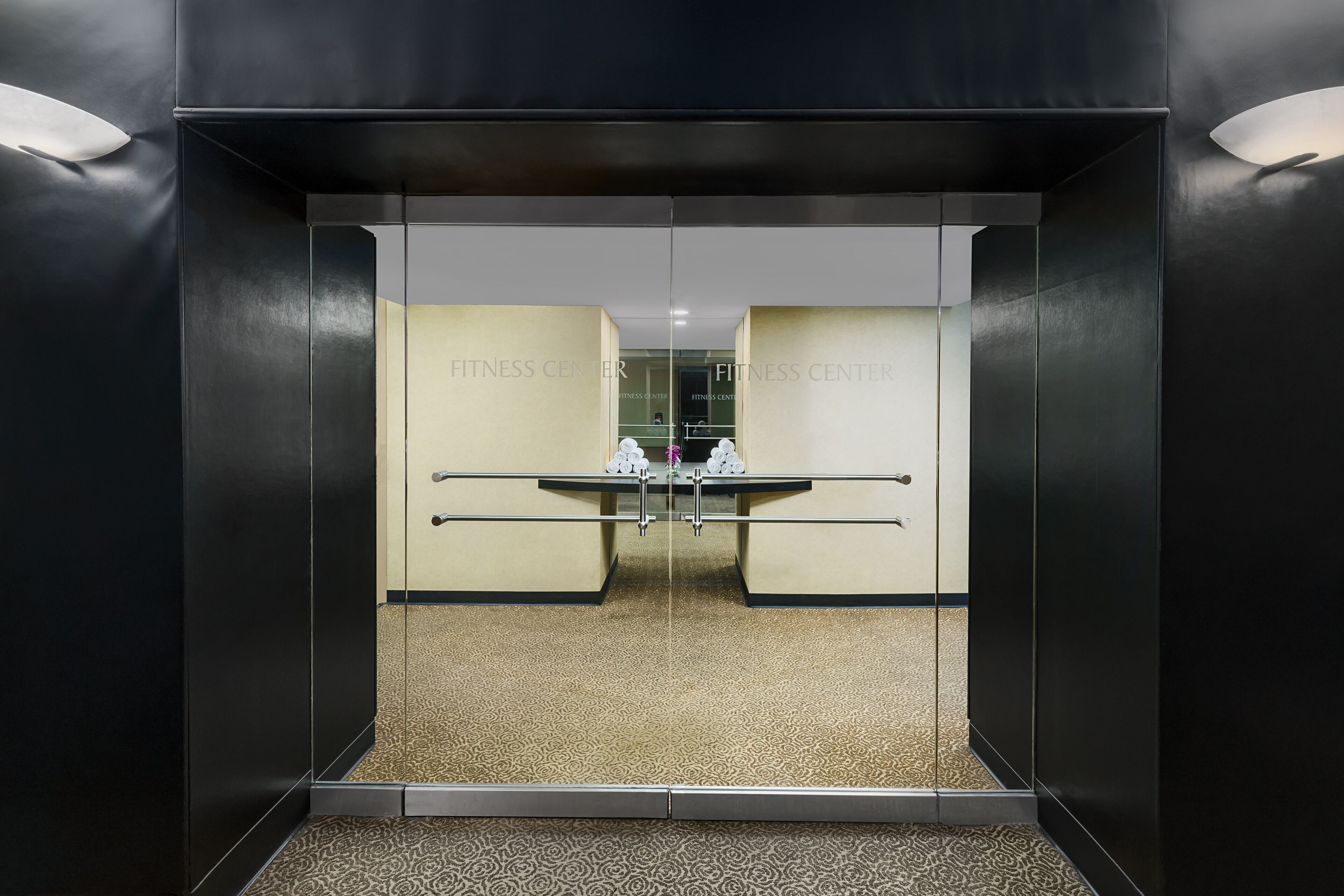 Un ascensor con un muro espejado que refleja un gimnasio.