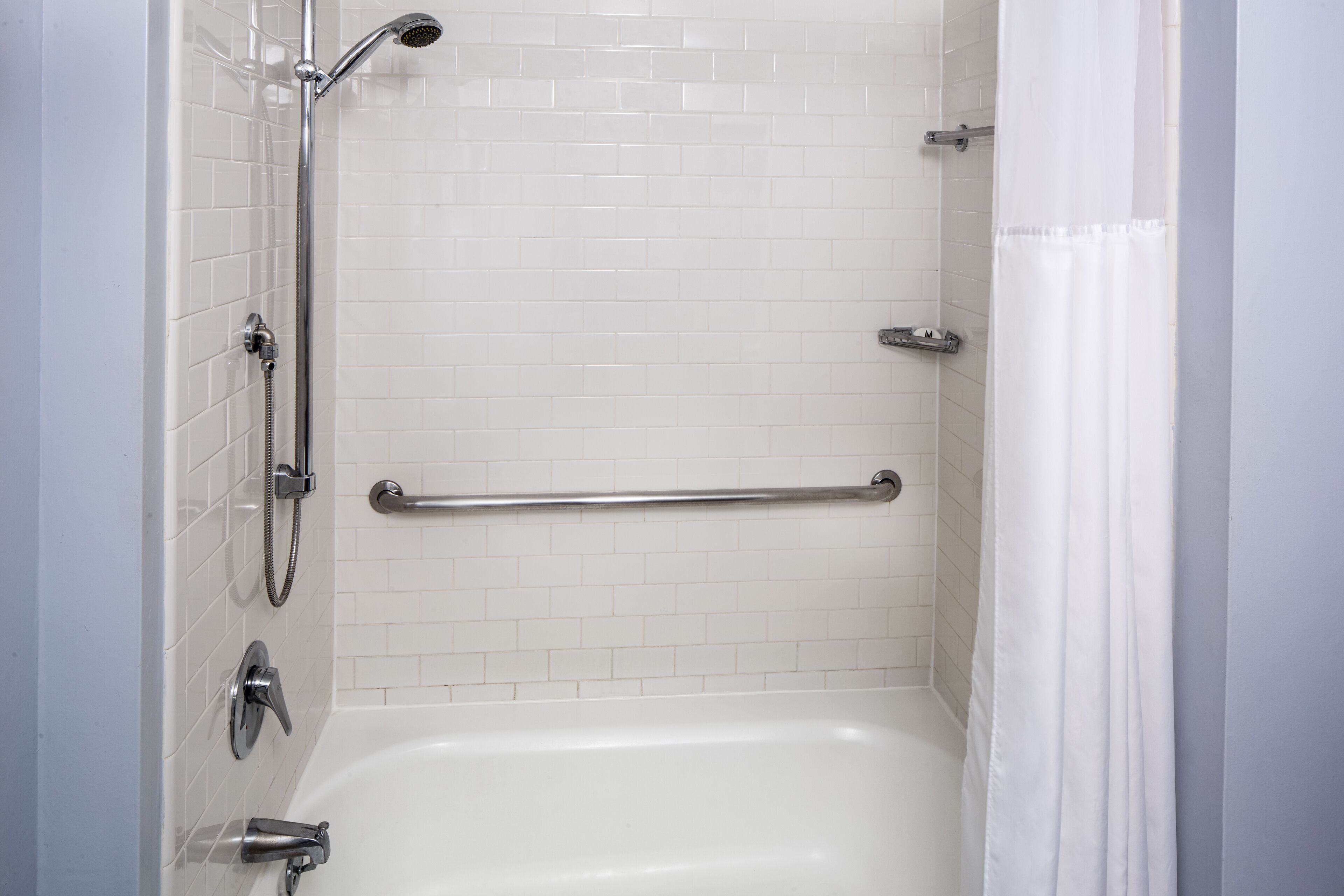 A bathroom with a white bathtub, a shower with a handheld showerhead, and a grab bar installed for safety.