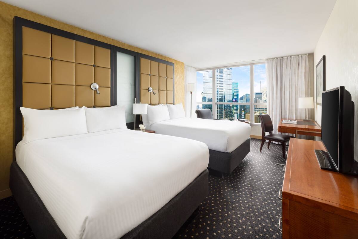 A hotel room with two beds, a desk, a TV, and a city view.