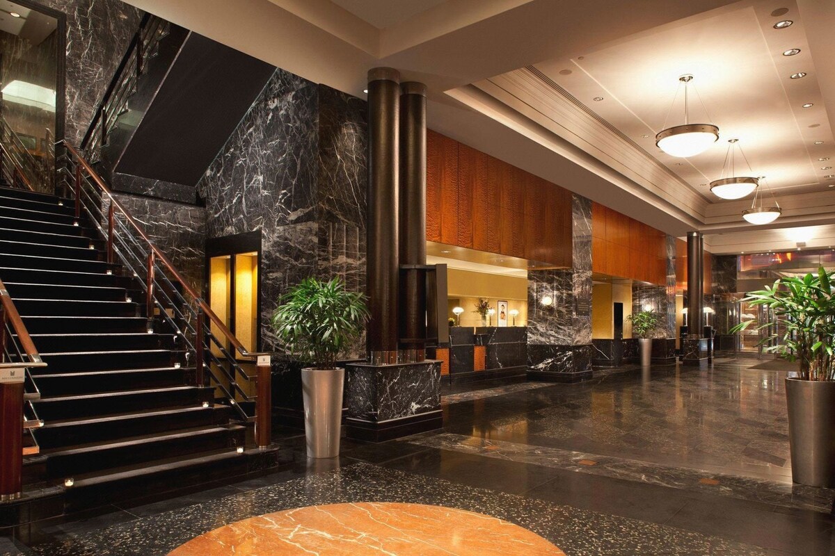 A lobby with a marble staircase, a reception desk, and potted plants.