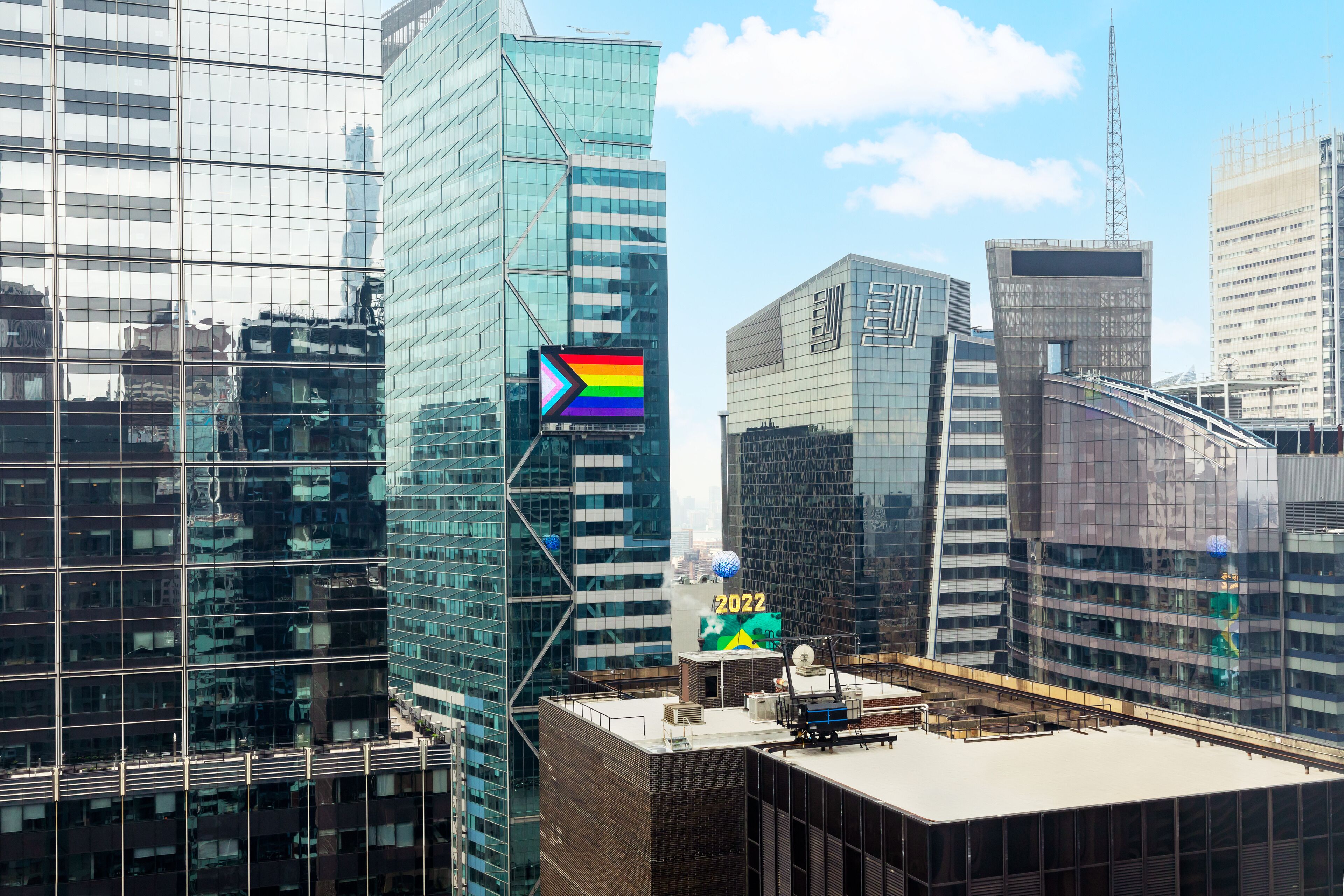 A modern cityscape with high-rise buildings, including a prominent glass skyscraper with a rainbow flag and the year 2022 displayed.