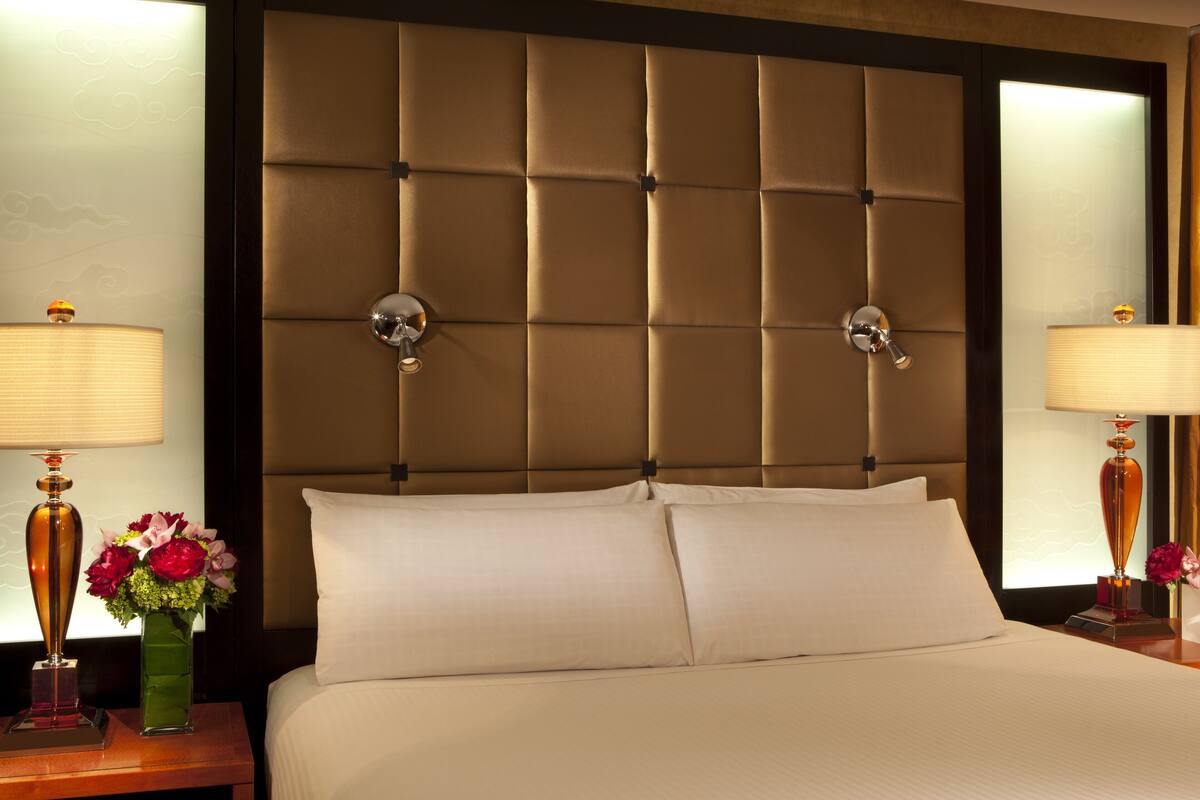 A hotel room with a tufted headboard, two bedside lamps, a vase of flowers, and a neatly made bed.