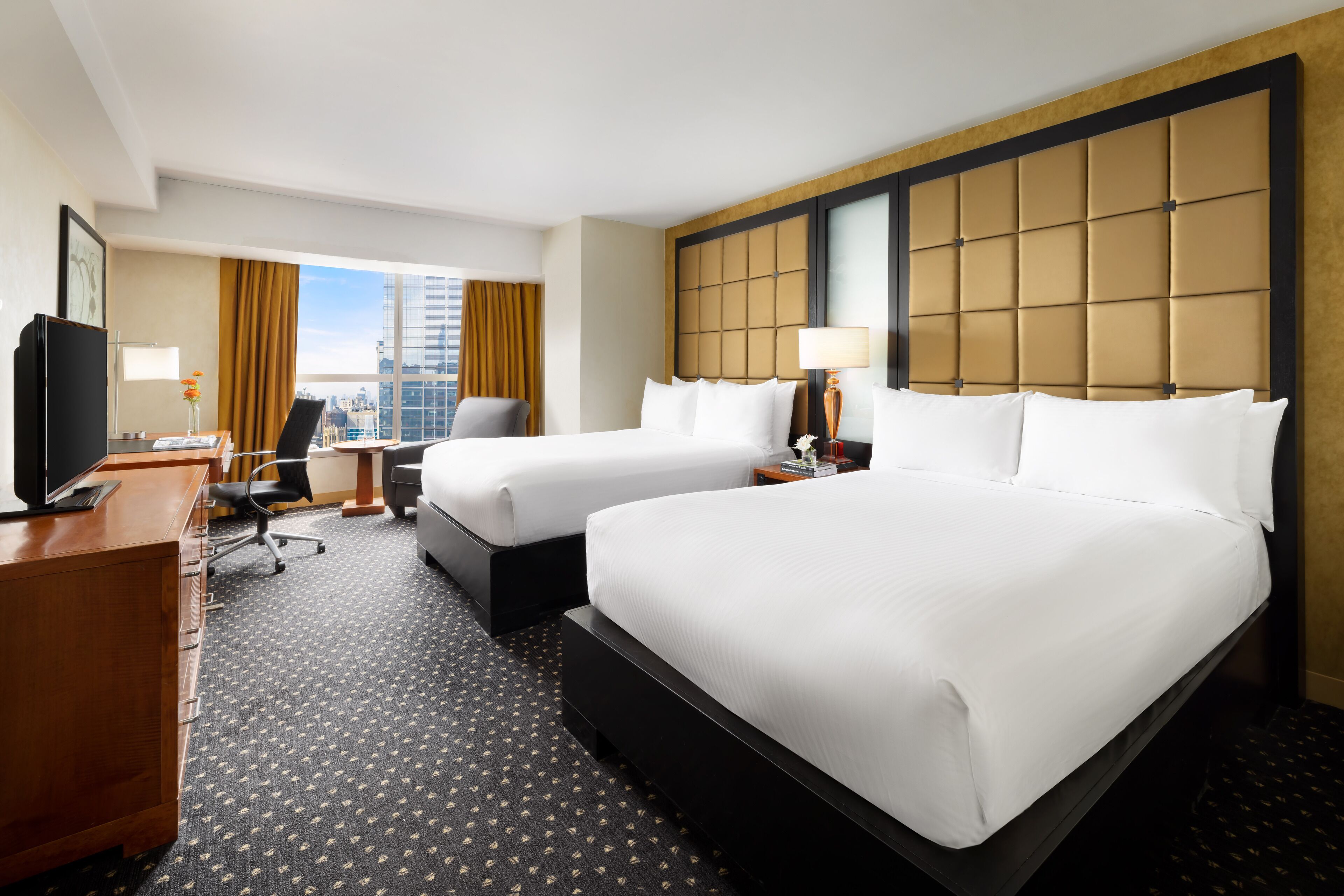 A hotel room with two beds, a desk, a chair, a TV, and a city view.