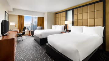 A hotel room with two beds, a desk, a chair, a TV, and a city view.