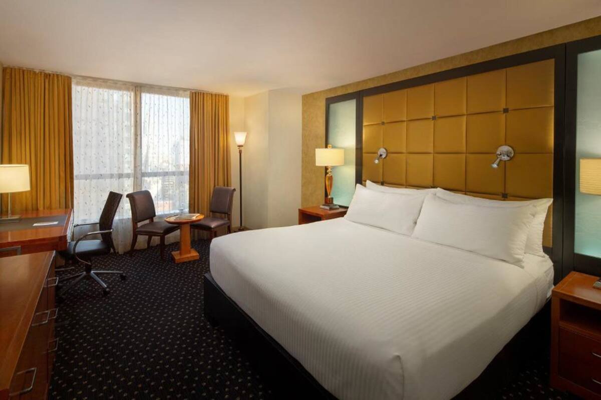 A hotel room with a large bed, a desk with a chair, a small table, and a lamp.