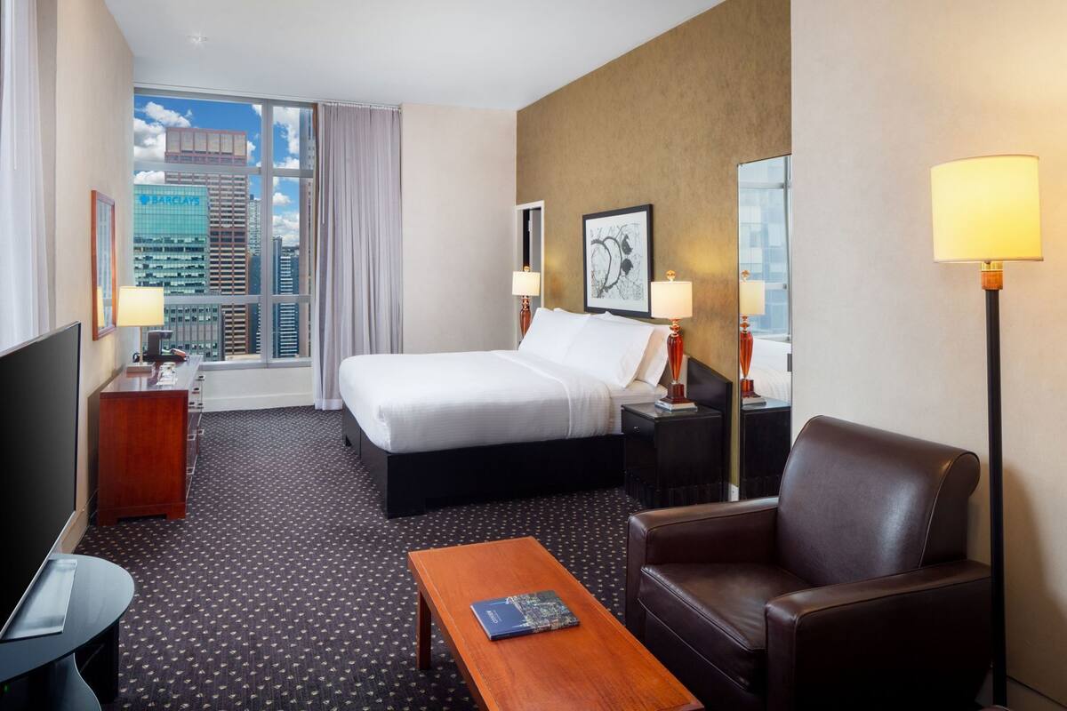 A hotel room with a bed, a desk, a chair, a coffee table, and a TV.