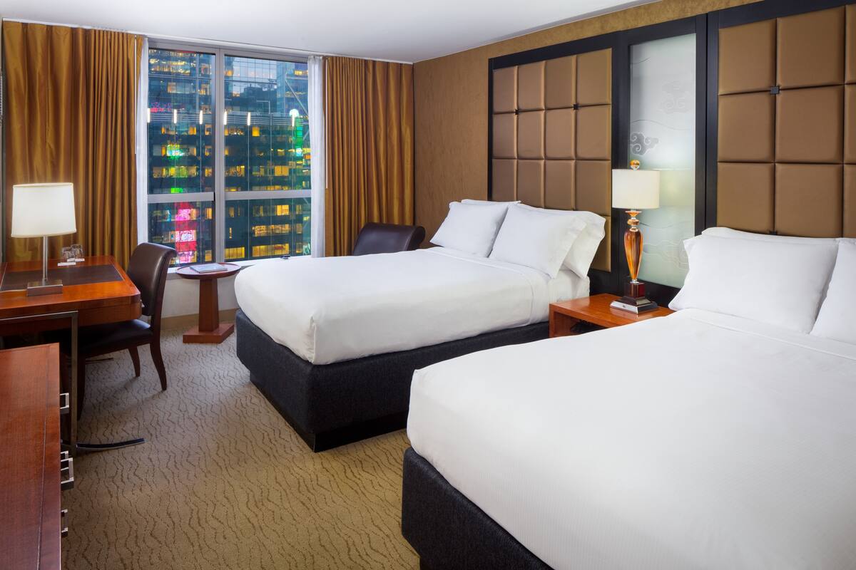 A hotel room with two beds, a desk, and a chair.
