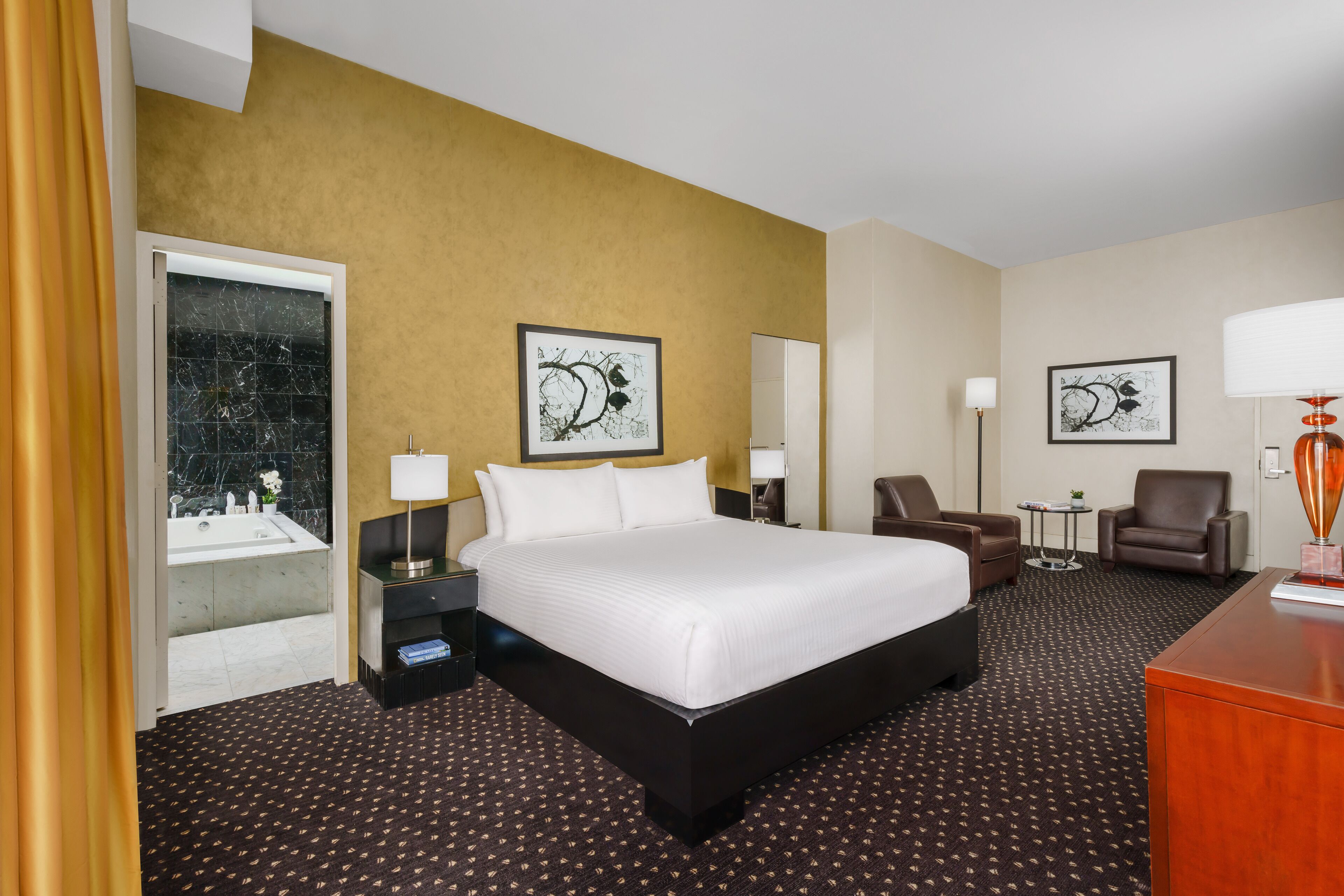 A hotel room with a large bed, two armchairs, a desk, and artwork on the walls.