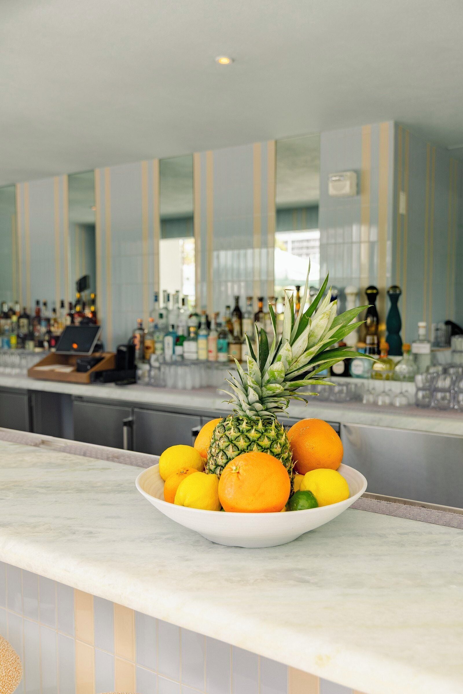 A bar area with a bowl of fruit on the counter, including pineapple and oranges.