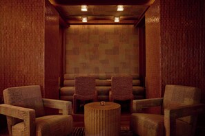 A room with a patterned brick wall, two armchairs, a round wooden table, and a ceiling with recessed lighting.