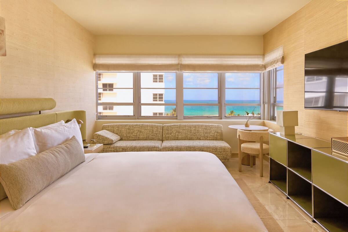 A hotel room with a large bed, a sofa, a small table, and a TV.