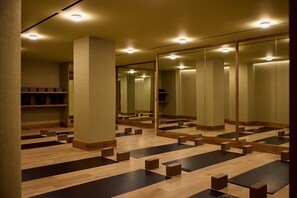 A yoga studio with wooden floors, black yoga mats, and wooden blocks.