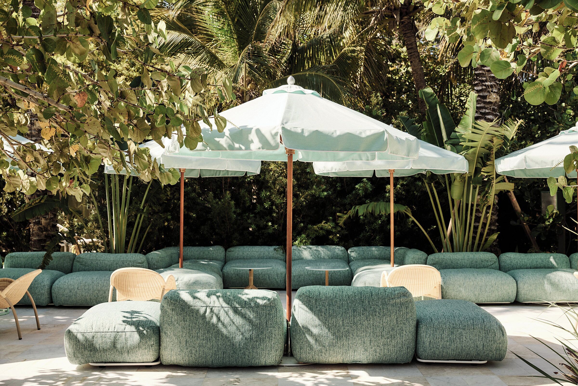 A seating area with green upholstered sofas and white umbrellas, surrounded by lush greenery.