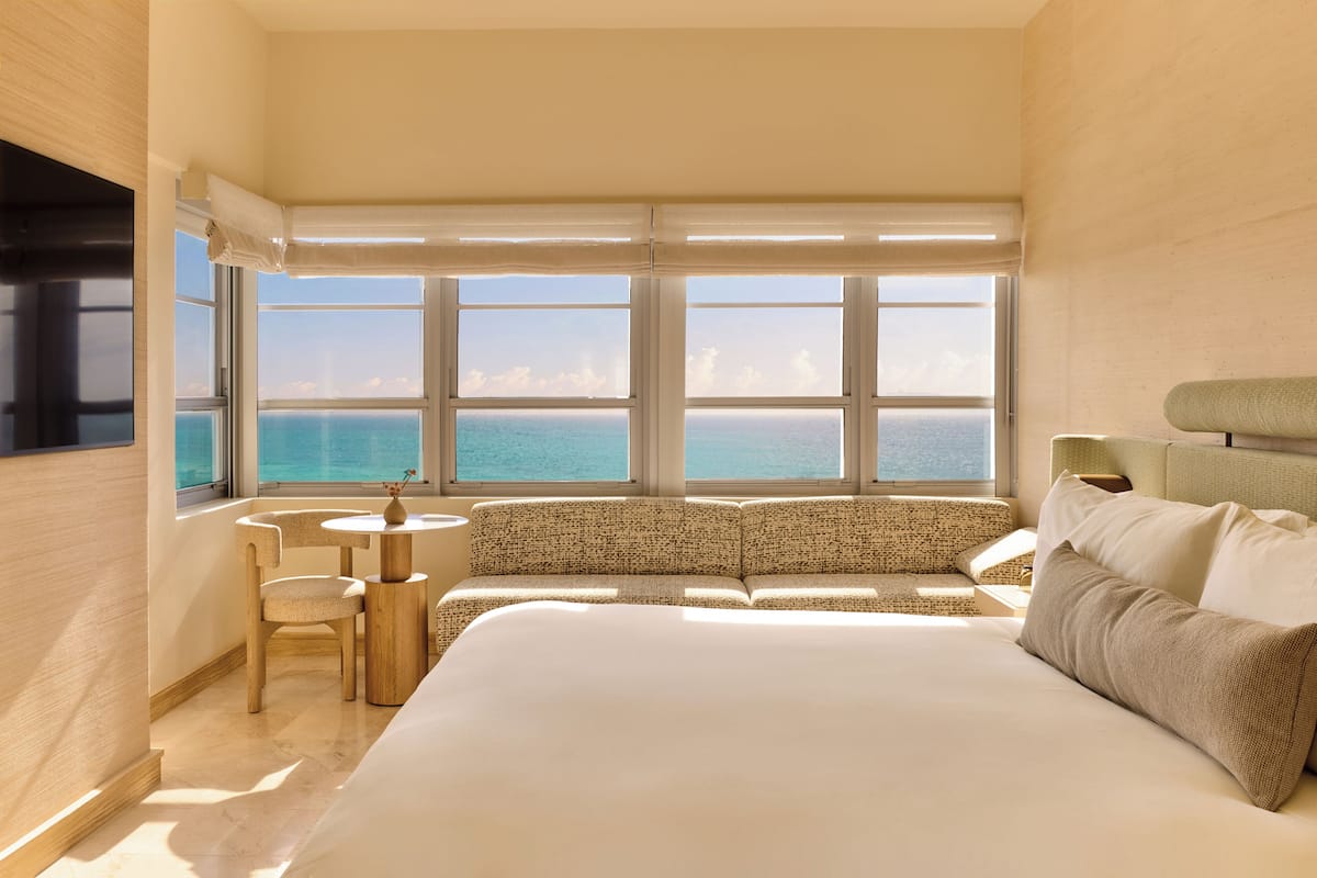 A hotel room with a large bed, a seating area, and a view of the ocean.
