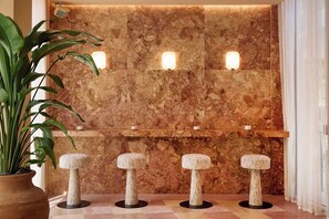 A reception area with a marble wall, three illuminated wall sconces, a potted plant, and three stools.