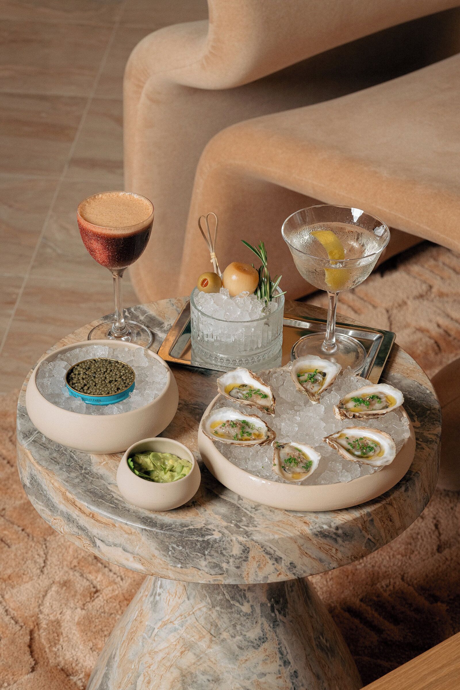 A marble table with a seafood platter, two glasses of wine, and a small bowl of green sauce.