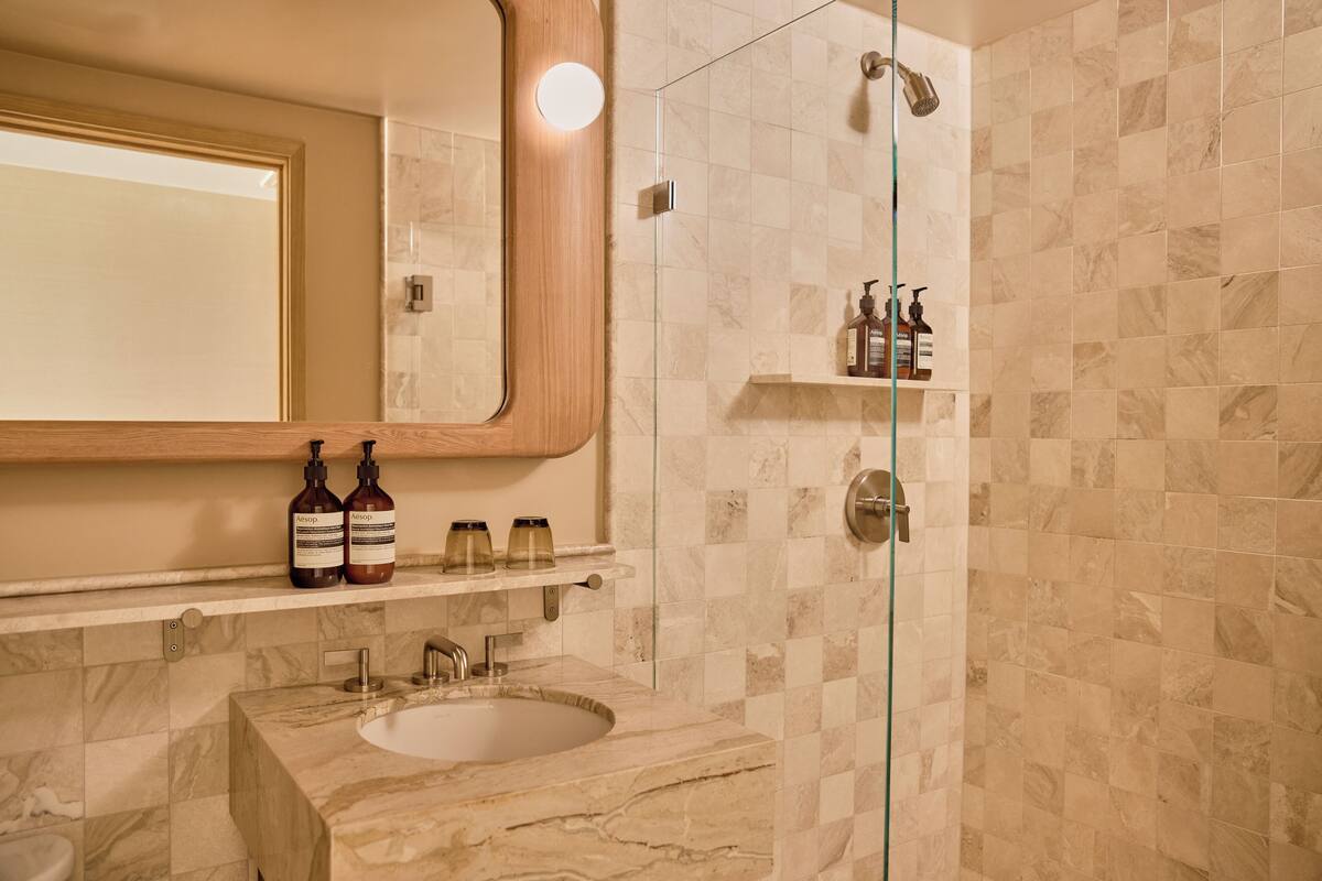 A bathroom with a marble sink, a glass-enclosed shower, and a shelf with toiletries.