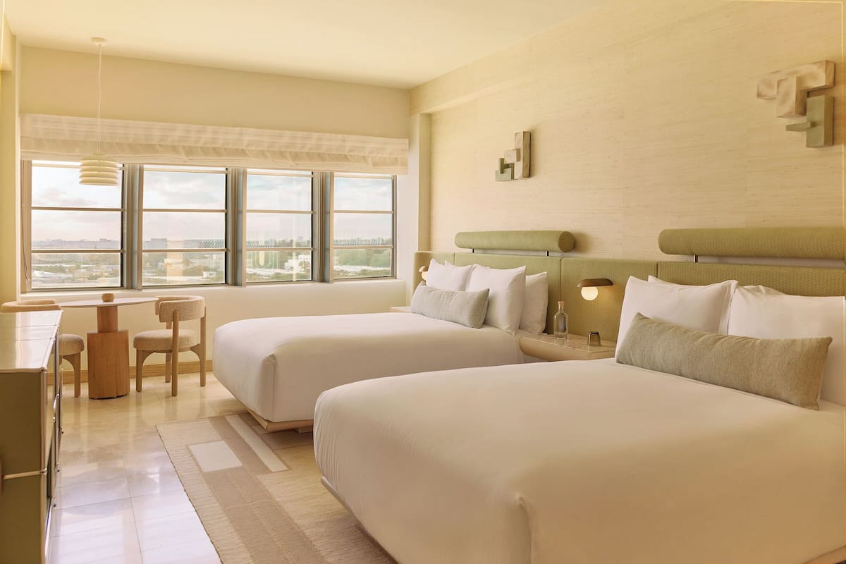 A hotel room with two beds, a desk, and a view of the city.