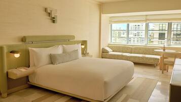 Habitación de hotel con una cama grande, un sofá, una mesita y un ventanal con vistas a la ciudad.