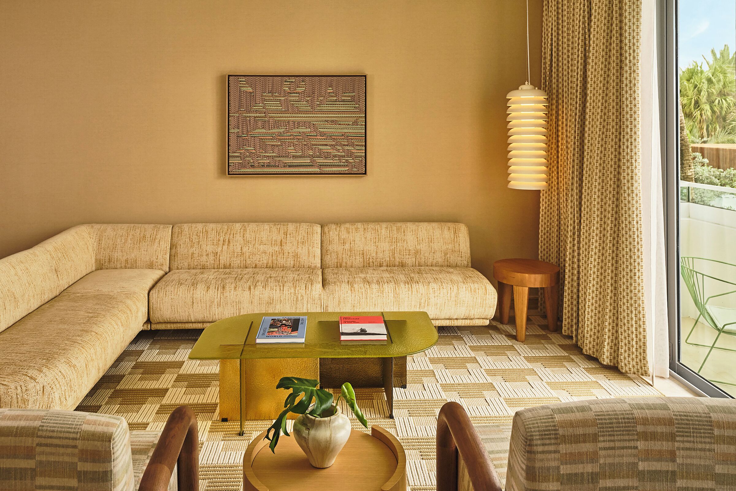 Un salon avec un canapé beige, une table basse en verre ornée d’une plante et une œuvre d’art encadrée accrochée au mur.