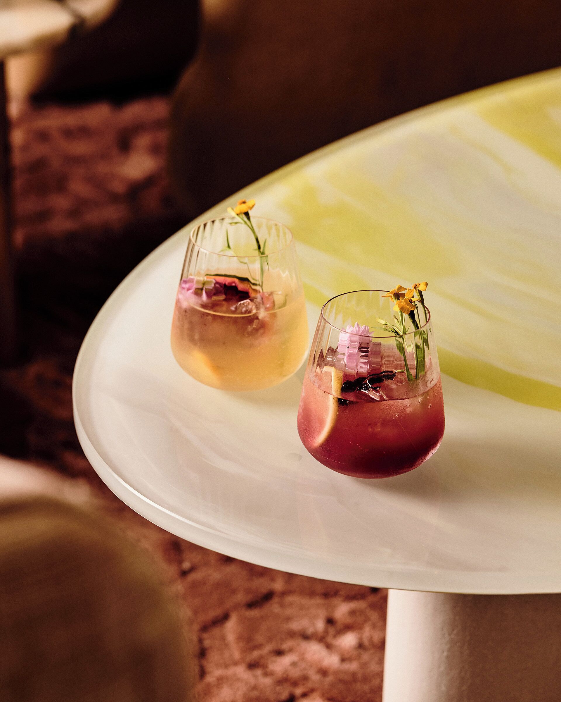 Deux verres de cocktails sur une table blanche, avec un fond jaune.