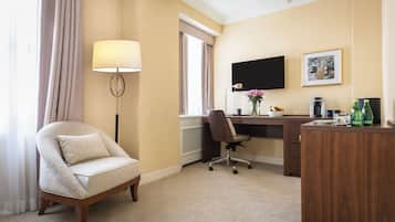 Camera d'albergo con una poltrona beige, una scrivania con un computer, una televisione a schermo piatto, una macchina del caffè e un tavolino con delle bottiglie.