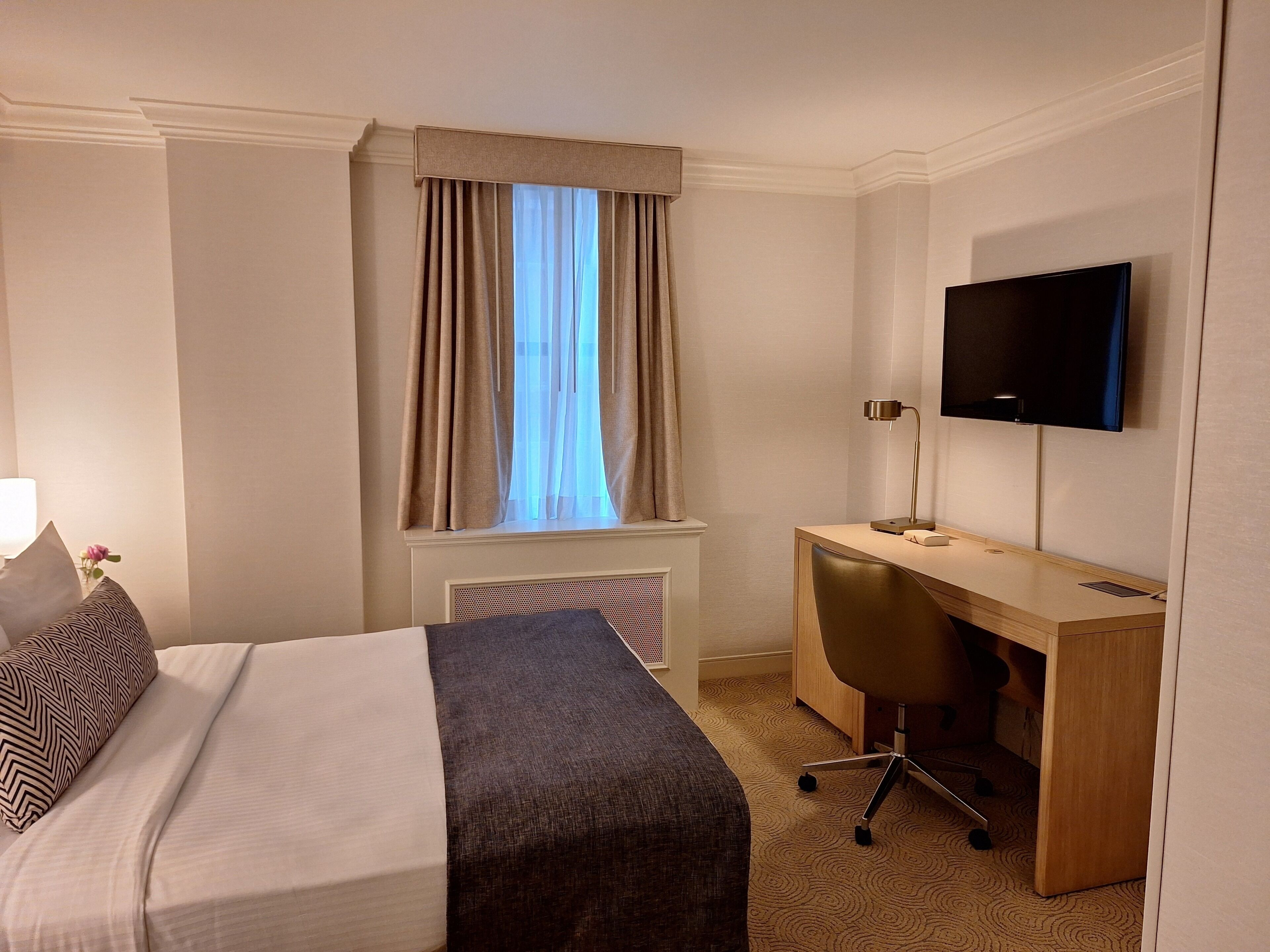 A hotel room with a bed, a desk, a chair, a television, and a window with curtains.