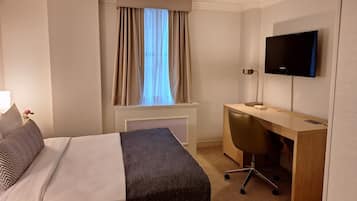 A hotel room with a bed, a desk, a chair, a television, and a window with curtains.