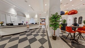 Un vestíbulo de hotel con mostrador de recepción, zona de estar y una planta grande en maceta.