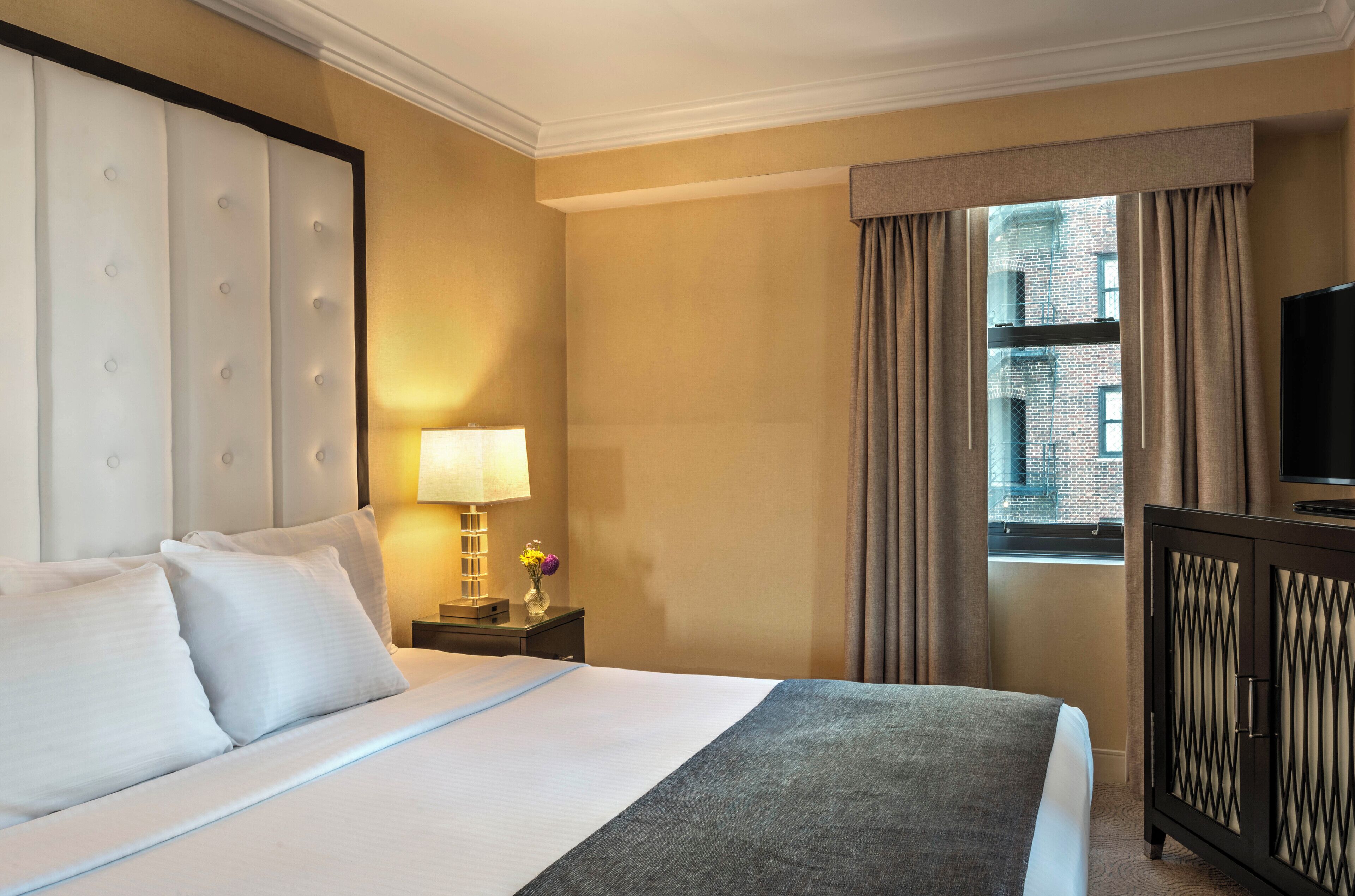 Ein Hotelzimmer mit einem großen Bett, einem Nachttisch mit Lampe, einem Schminktisch und einem Fernseher.