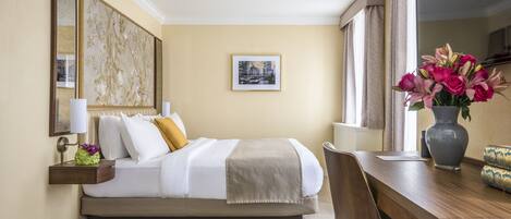 Een hotelkamer met een bed, nachtkastje, lamp en een vaas met bloemen.