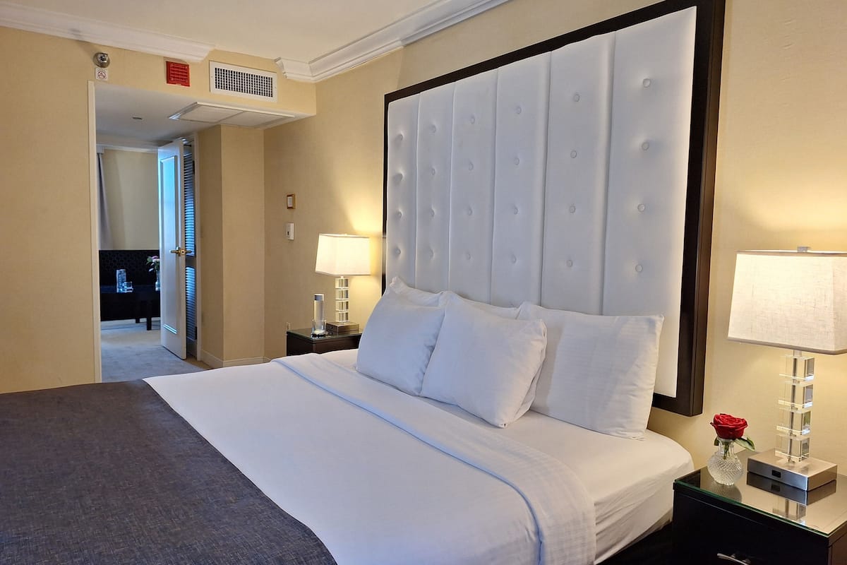 A hotel room with a large bed, a nightstand with a lamp, and a view of the hallway.