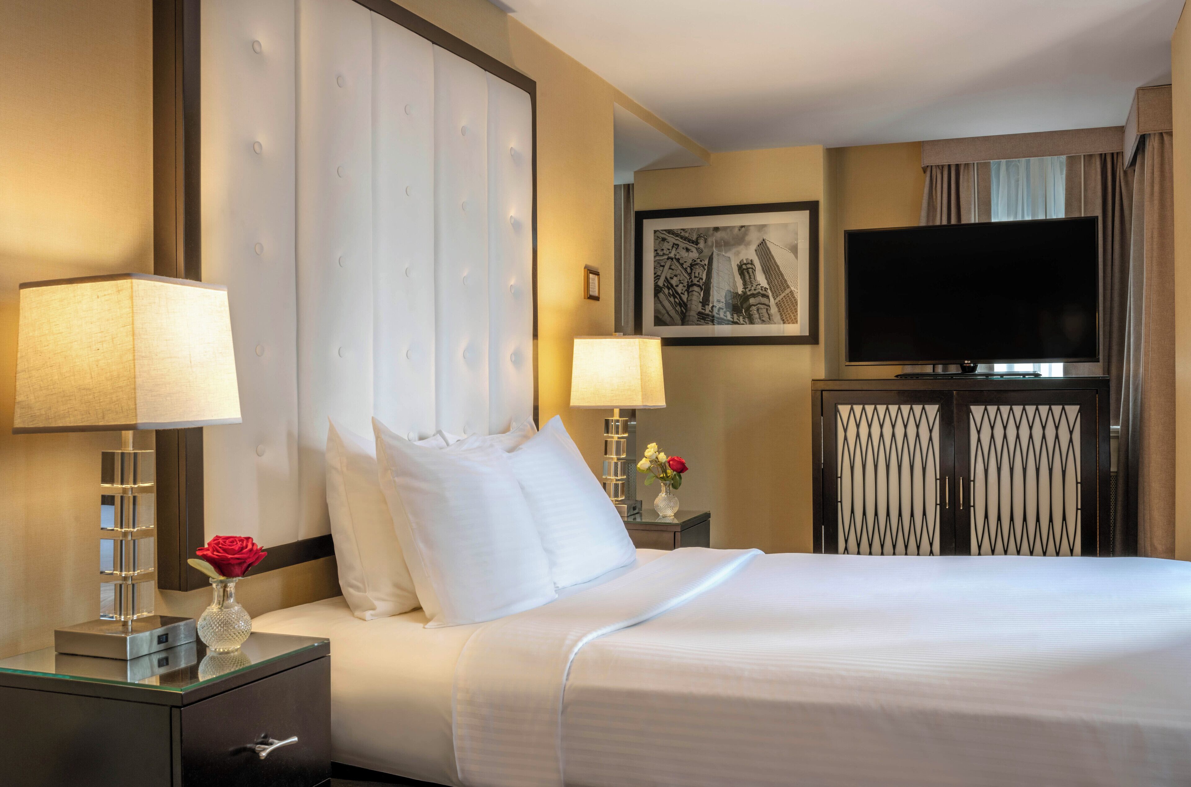 A hotel room with a large bed, two bedside tables with lamps, a flat-screen TV, and a framed picture on the wall.