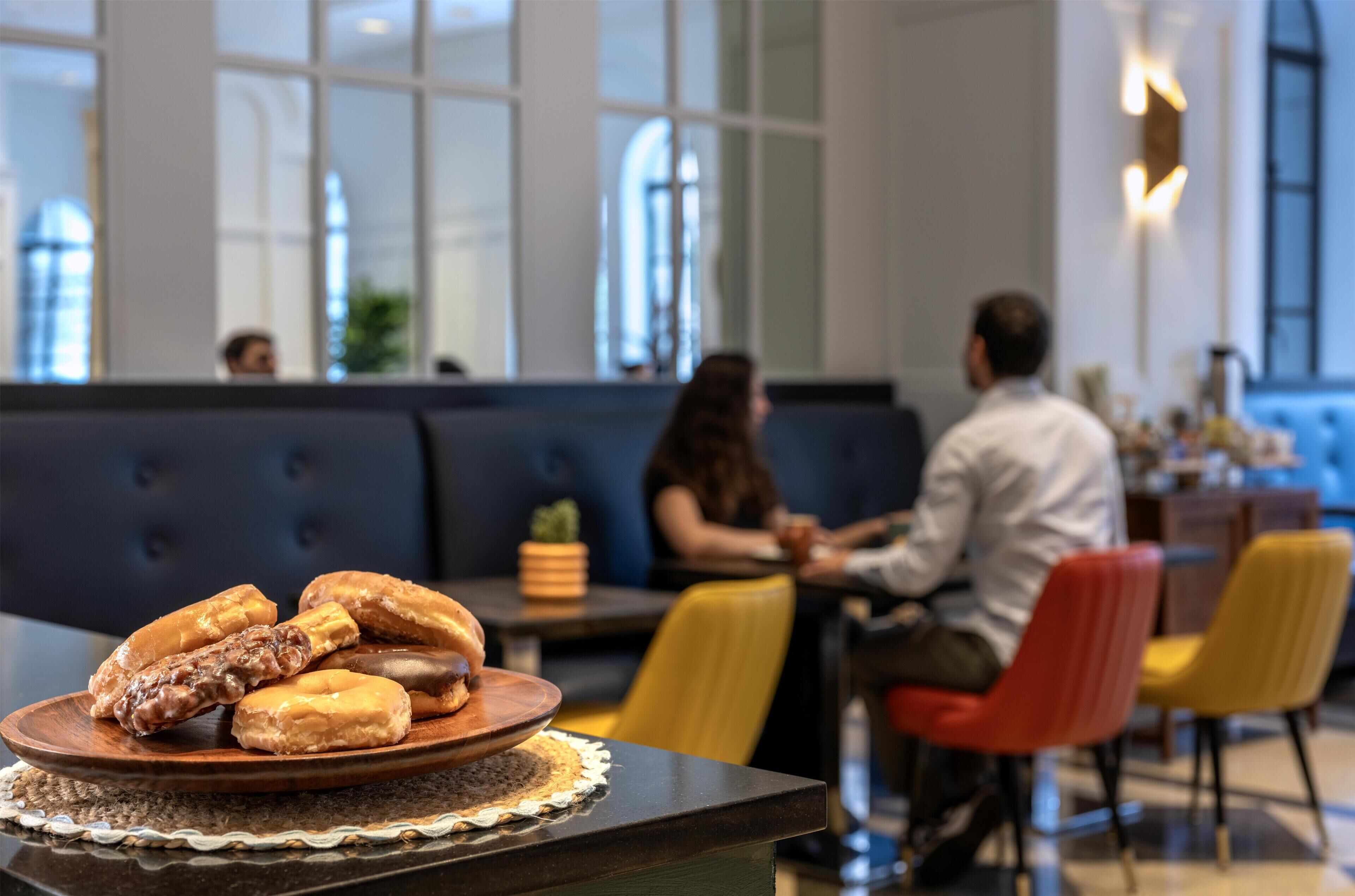 A dining area with a table displaying pastries, a seating area with a sofa and chairs, and a large window providing natural light.